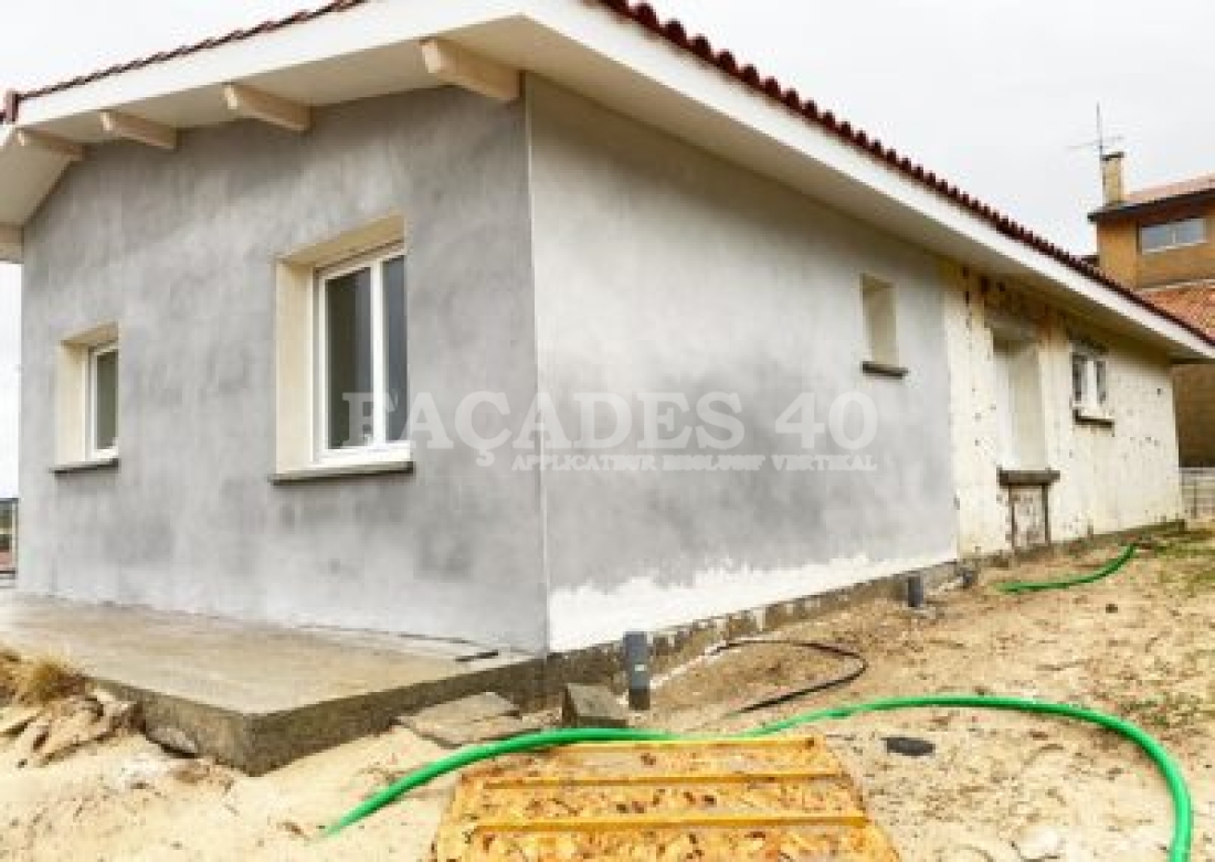 Maison en construction avec façade grise et tuyaux verts.